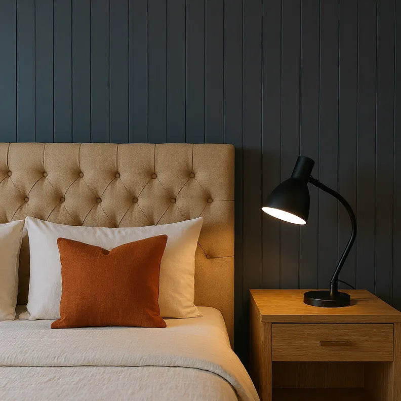 Bedroom with tufted headboard, pillows, and a lamp on a nightstand against a dark paneled wall.
